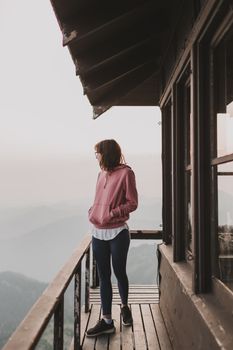 在华盛顿州阿什福德的山间阳台上，一位穿着粉红色连帽衫的女人凝视远方，拥抱着早晨的宁静