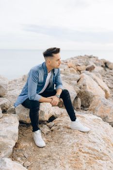 年轻人悠闲地坐在海边的岩石上，享受宁静的户外时光