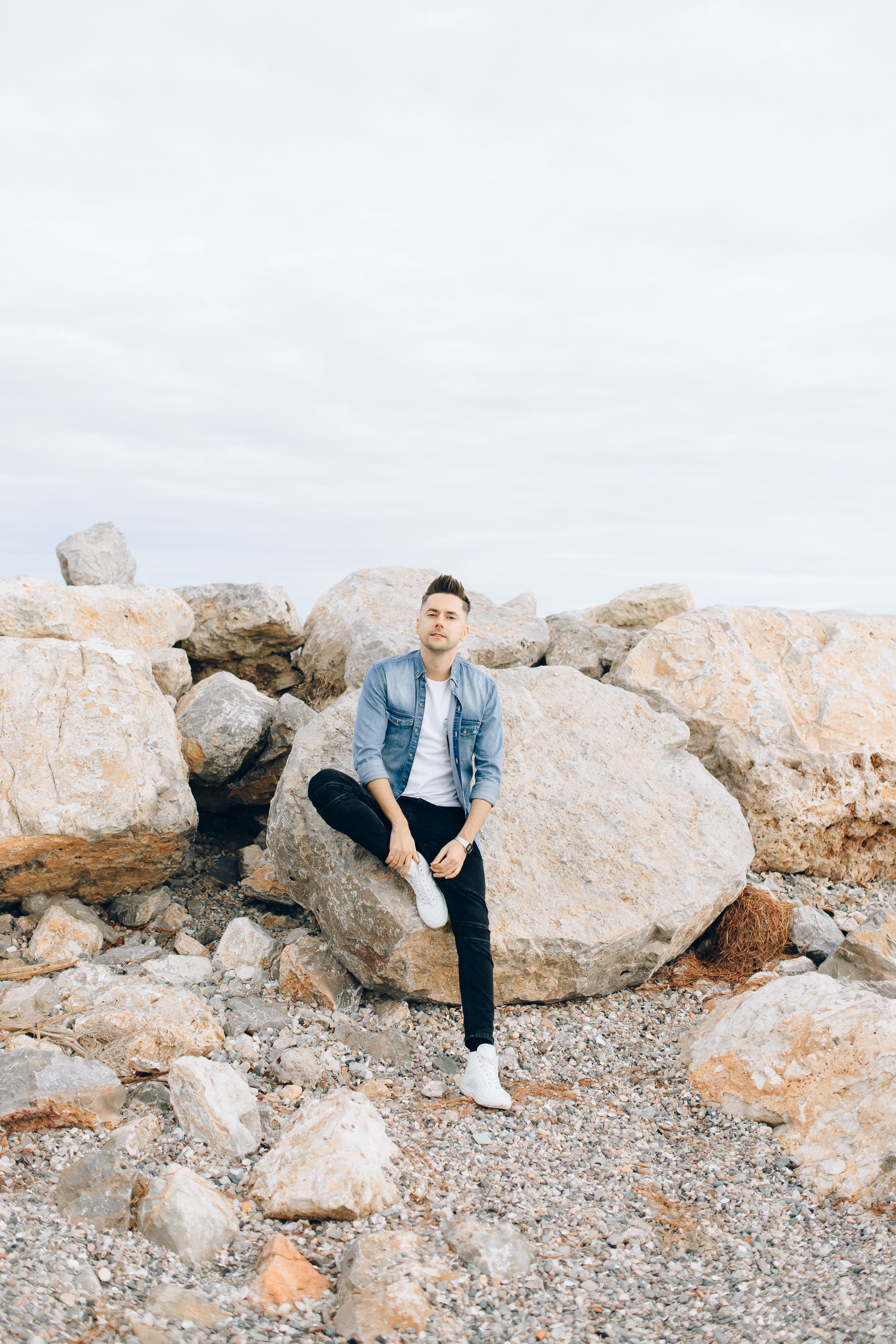 A Man Wearing a Denim Jacket Sitting on a Big Rock · Free Stock Photo
