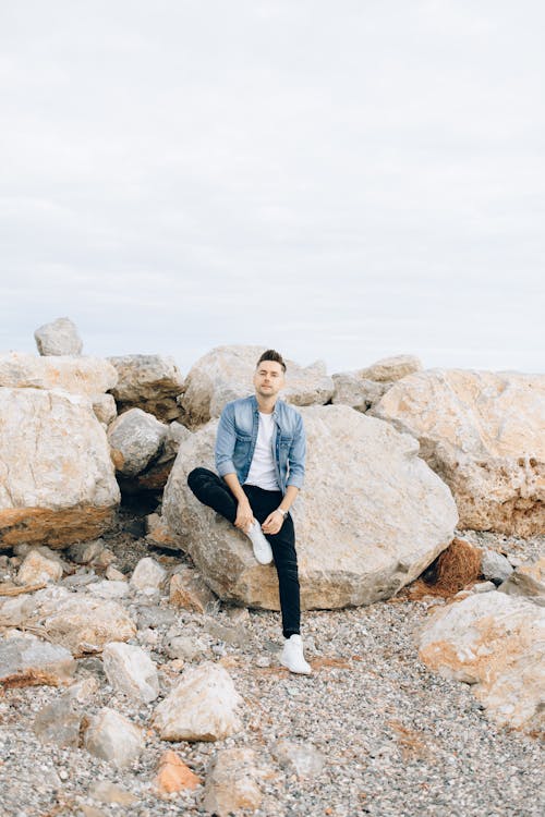 A Man Wearing a Denim Jacket Sitting on a Big Rock