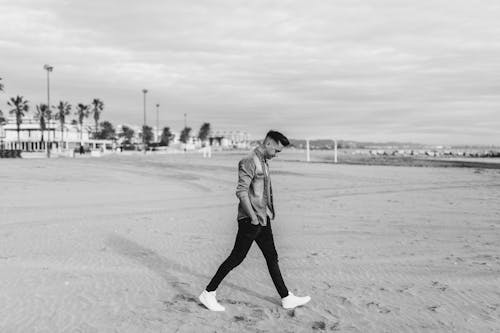 Grayscale Photo of a Man Walking on the Beach
