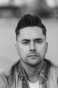 一张表情严肃的黑白特写肖像，描绘的是一位年轻成年男子