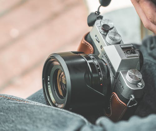 Selective focus of retro photo camera with blend on lens on legs of unrecognizable person on blurred background