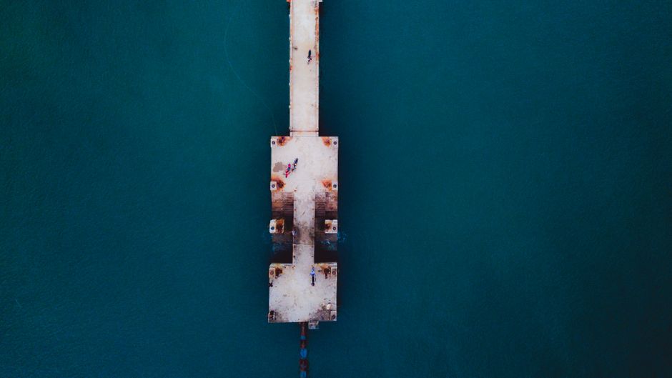 Drone view of long old shabby pier above vibrant calm dark blue ocean in daylight
