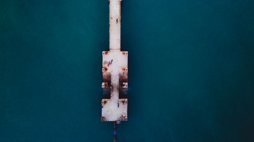 Free Drone view of long old shabby pier above vibrant calm dark blue ocean in daylight Stock Photo