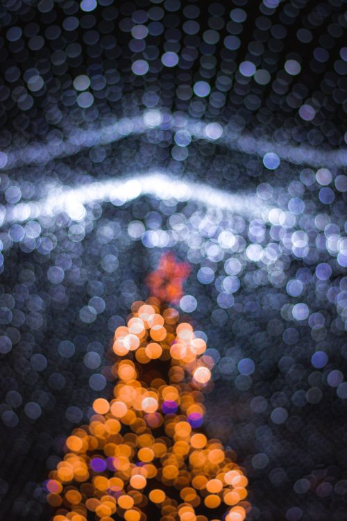 Free Blurred bokeh view of an illuminated Christmas tree against a night sky creating a festive and artistic ambiance. Stock Photo
