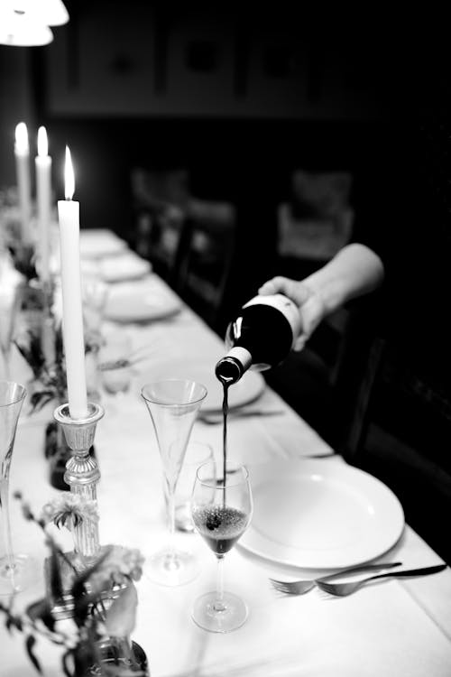 Free Black and white person pouring wine in transparent glass on holiday table decorated with candles Stock Photo