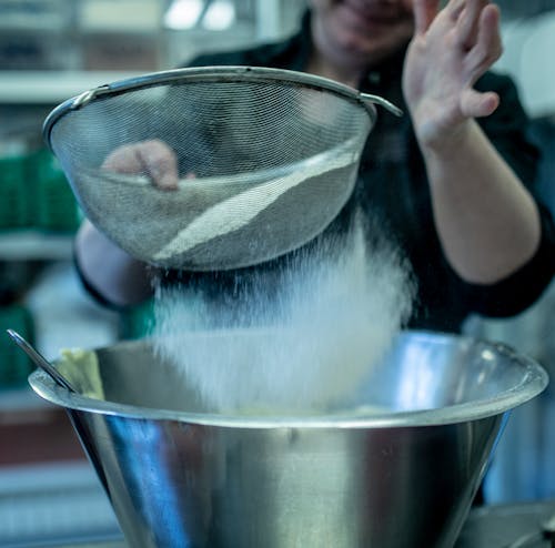 Faceless professional female cook in black clothing sifting flour through sieve while working in restaurant