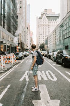 一个男人背着背包，站在纽约市一条繁忙的街道上，周围是汽车和摩天大楼
