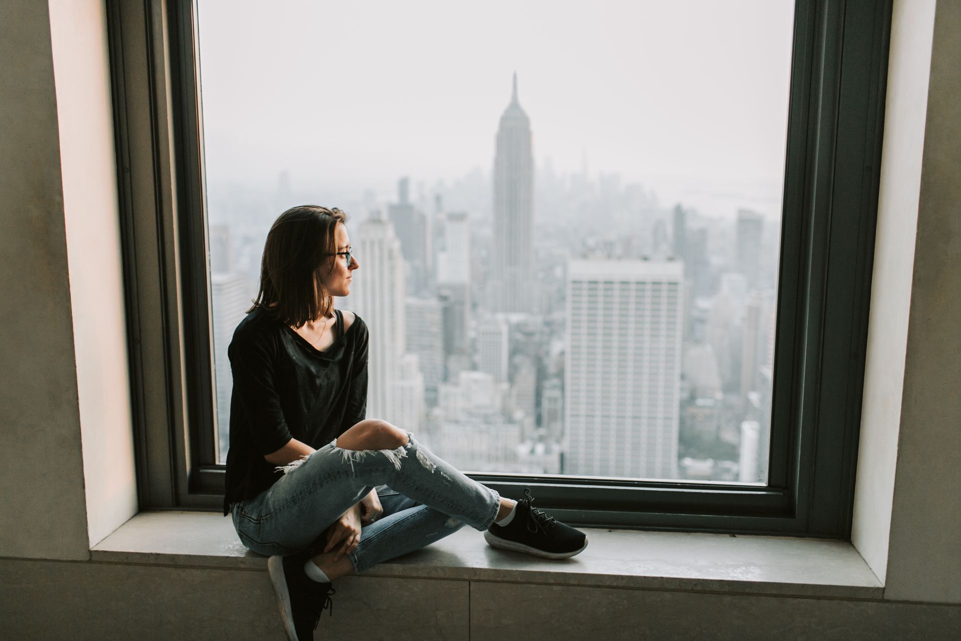 Woman in Black Jacket and Blue Denim Jeans Sitting on Window with the View on Empire State Building