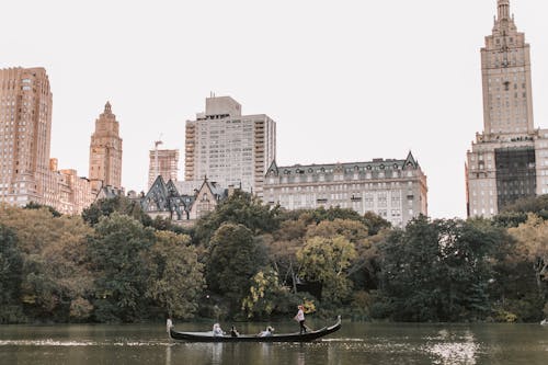 Free People on Boat on River in Central Park Beside Buildings Stock Photo