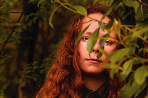 Free Portrait of a redhead woman partially covered by leaves, evoking mystery and nature. Stock Photo