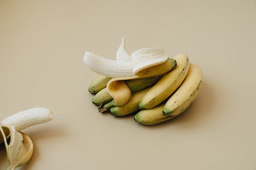 A bunch of ripe bananas with one peeled, displayed on a neutral backdrop. Ideal for food visuals.
