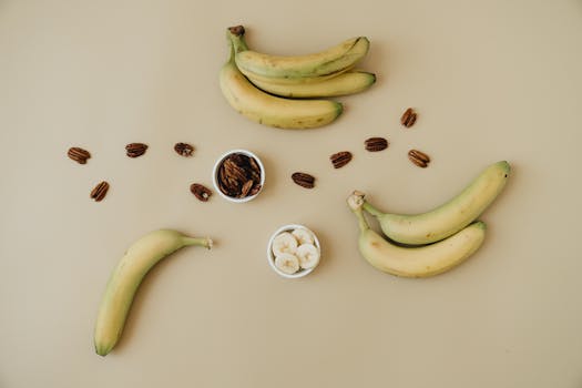 A top view of bananas and pecans artfully arranged on a minimalistic beige background, perfect for healthy eating concepts.
