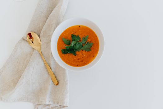Elegant bowl of carrot soup garnished with fresh herbs on a white background.