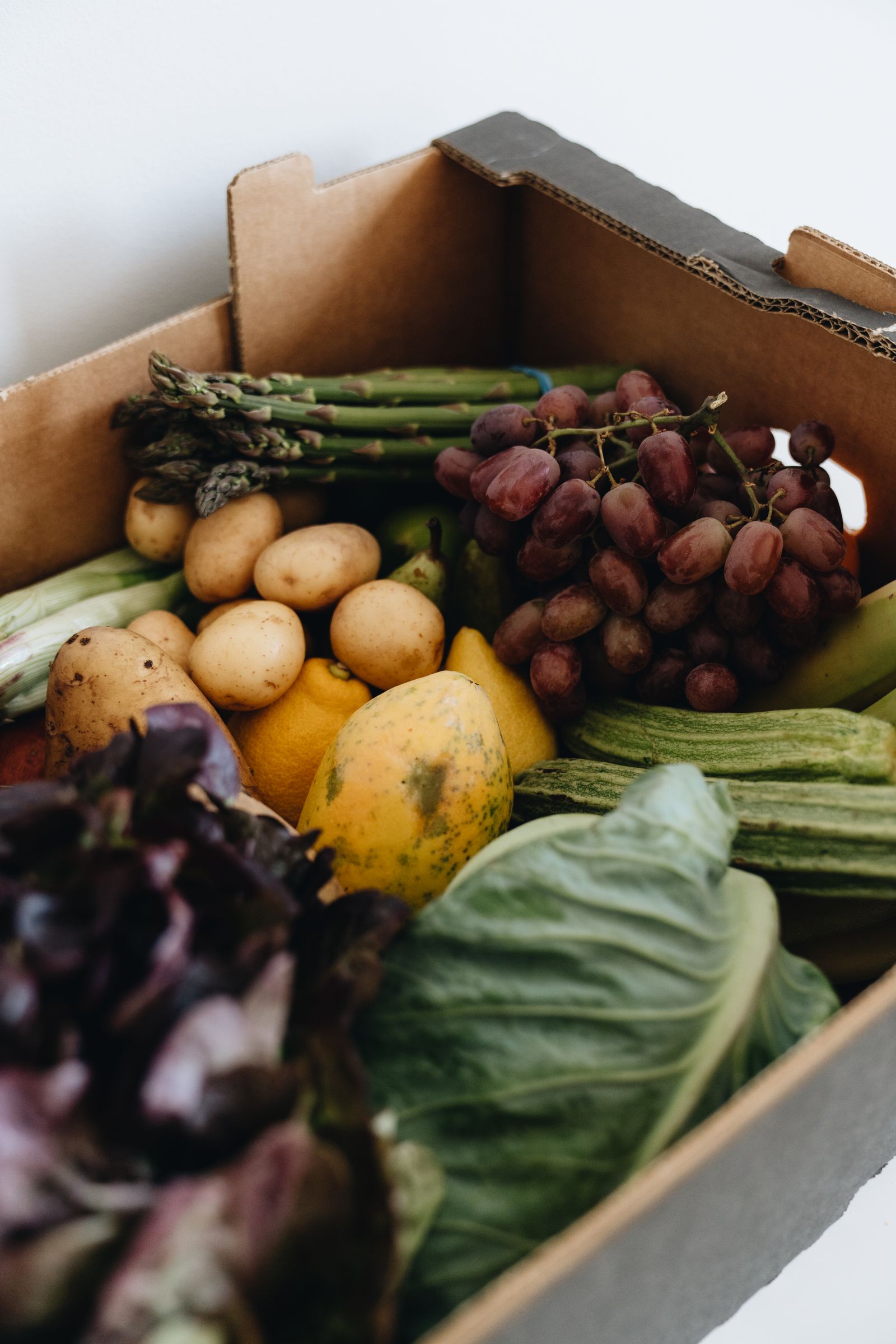 Box of fresh produce including potatoes, grapes, asparagus and cabbage