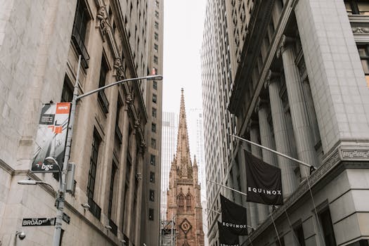 View of Trinity Church between skyscrapers on Broad Street, NYC, showcasing historic architecture.