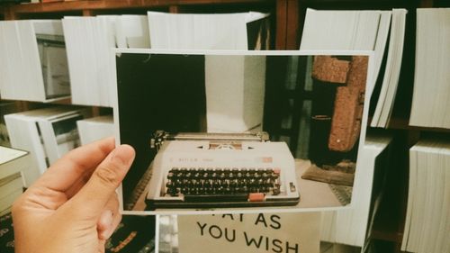 Free Hand holding a vintage photo of a retro typewriter amid shelves of books. Stock Photo