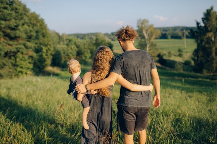 Back View Of A Family Walking On The Green Grass