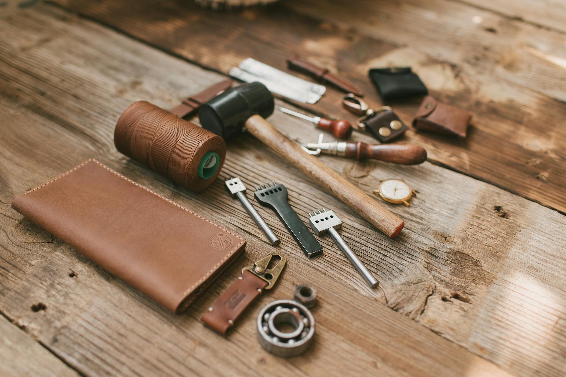 A Leather Wallet and Tools for Leather Crafting Lying on a Wooden Surface