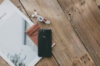 一张照片上，智能手机、耳机、皮套和日记本平放在木制表面上