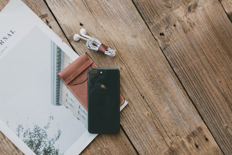 Black IPhone And Earphones Near Magazine On Wooden Surface