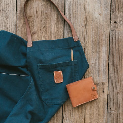 Apron with a Pencil in the Pocket and a Leather Wallet Lying on a Wooden Surface 