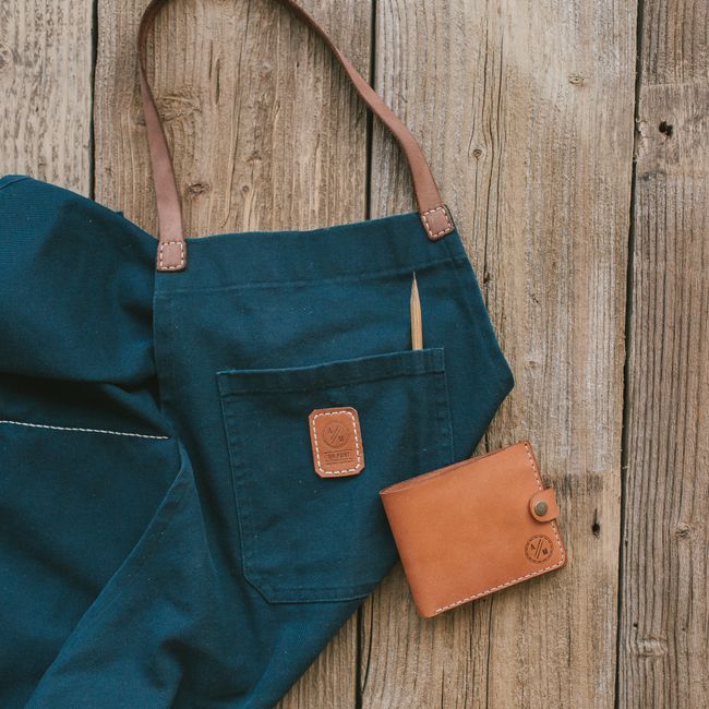 Handcrafted leather wallet and fabric apron on rustic wooden floor.