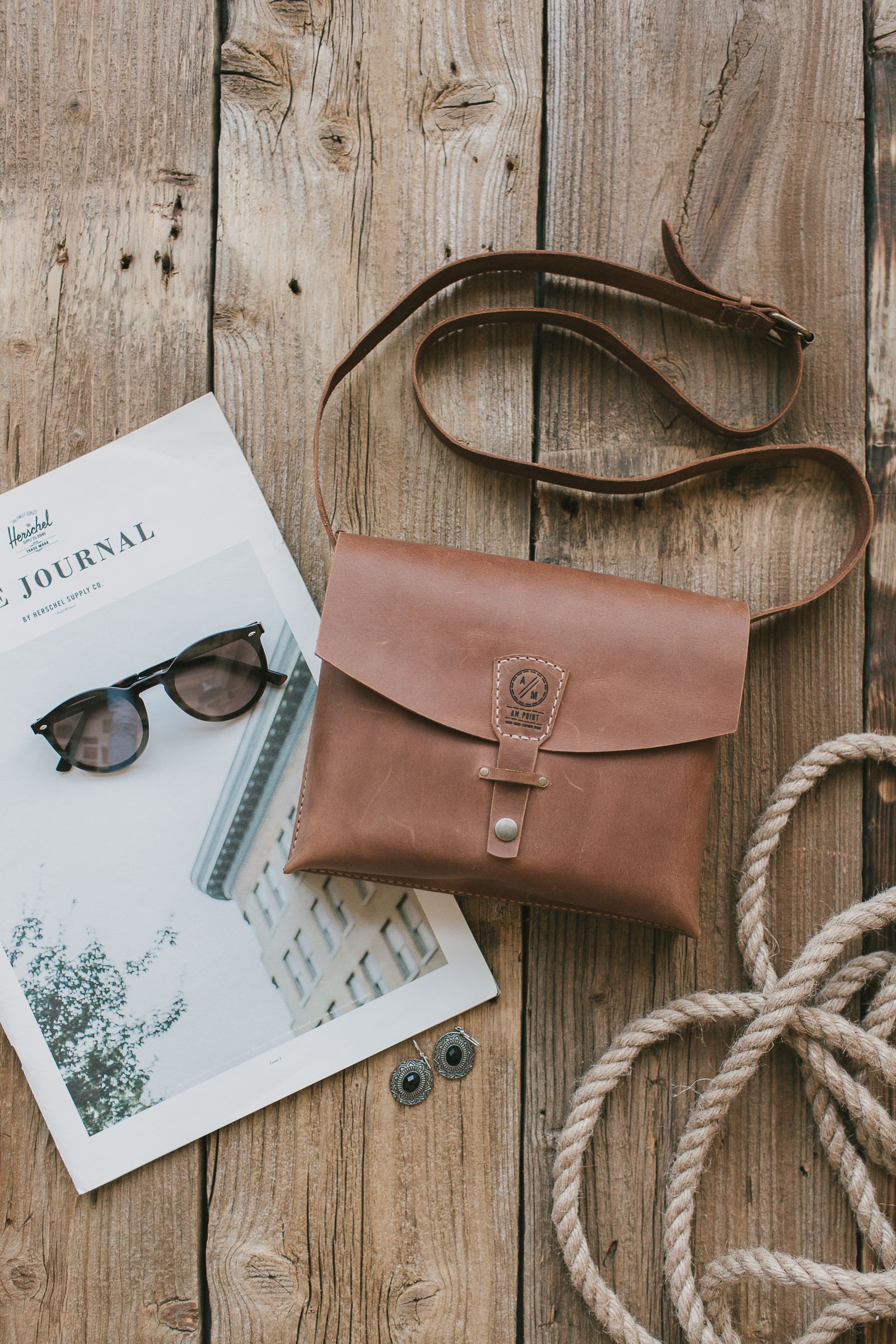 Brown vintage leather sling bag with sunglasses on a wooden table