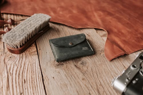 A Leather Wallet, Brush and a Film Camera Lying on a Wooden Surface 