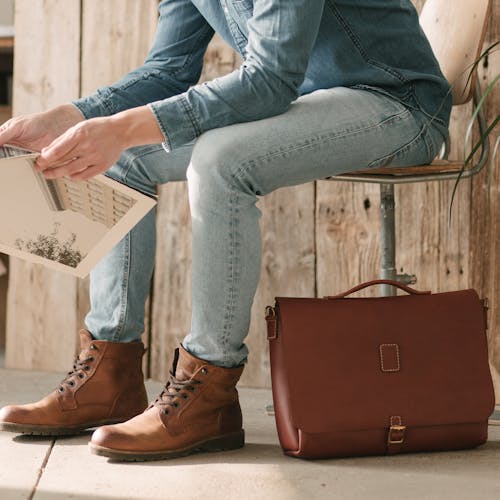 Free Person in Denim Clothes Sitting near the Brown Leather Briefcase Stock Photo