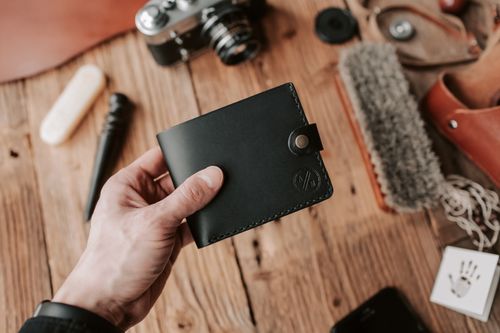 Free A hand holding a black leather wallet with camera and grooming tools on a wooden surface. Stock Photo