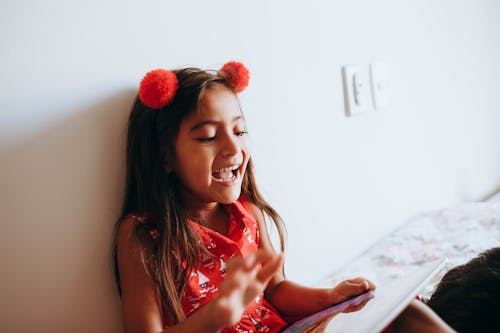 Photo of Girl Leaning on White Wall While Playing With Tablet Computer