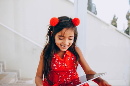 Free Delighted child in summer dress sitting on stairs and watching cartoon on modern tablet at weekend Stock Photo