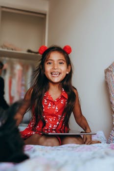Happy girl in red dress with tablet, smiling indoors. Bright expression captures pure joy.