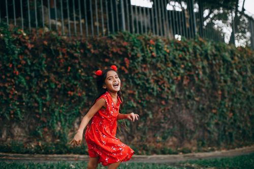 Free Side view of positive girl in dress running in park and looking at camera while having fun at weekend Stock Photo