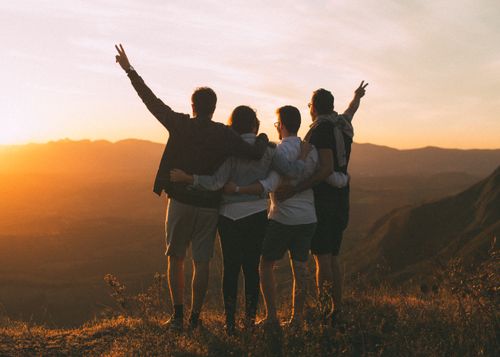 Free Full body back view of anonymous friends in casual clothes on grassy hill standing closely and embracing while admiring sundown in mountains Stock Photo