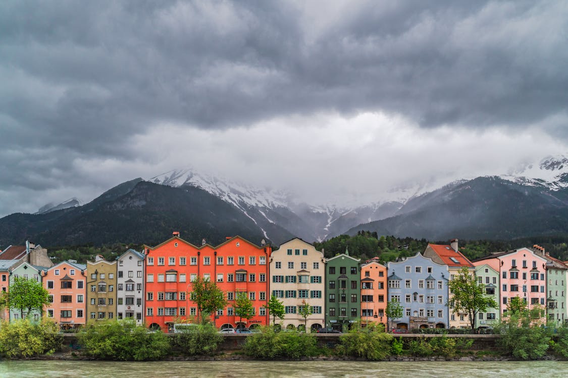 White and Brown Concrete Buildings Near Green Trees and Mountains Under White Clouds