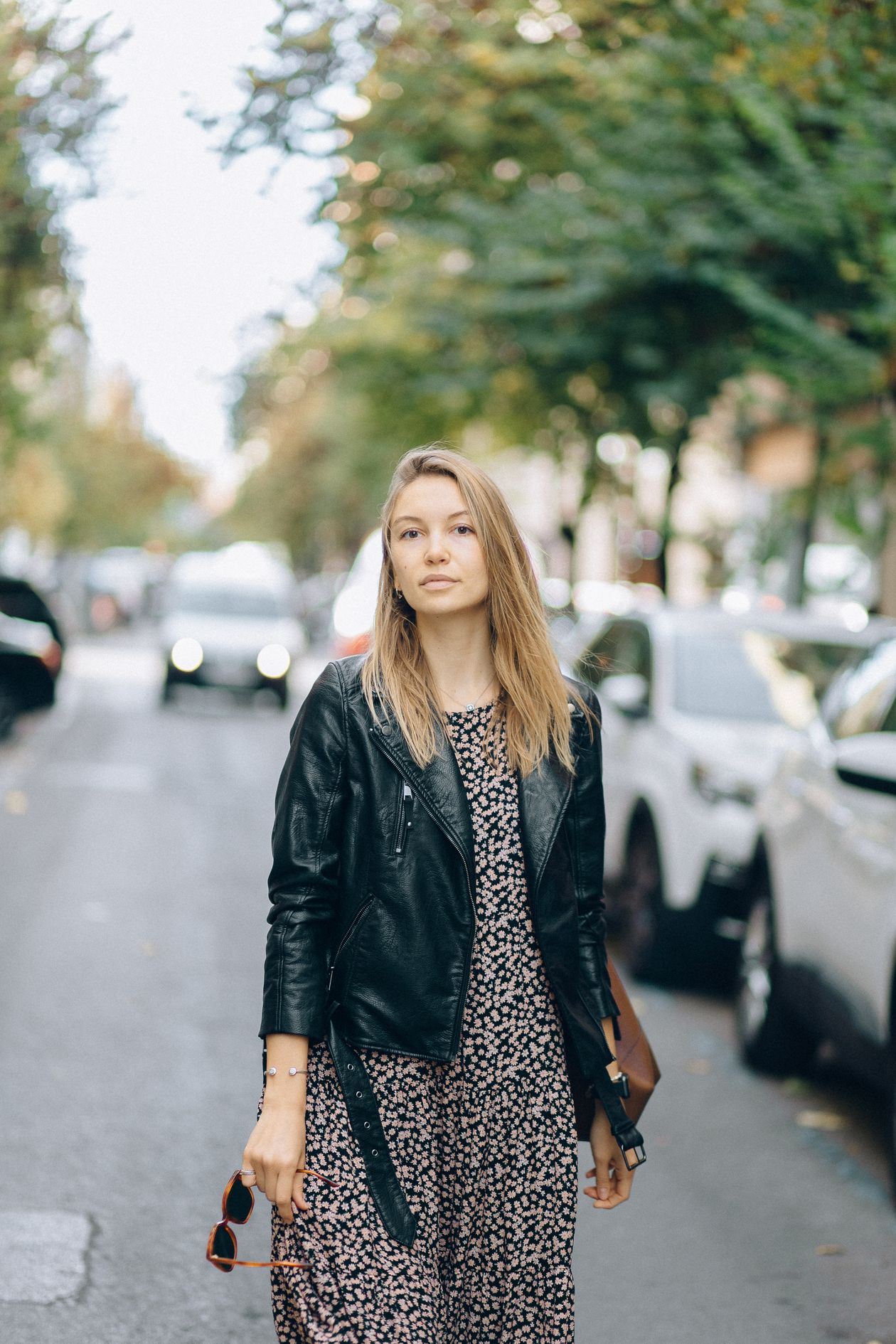 Woman in a black leather jacket over a dark floral dress on a city street