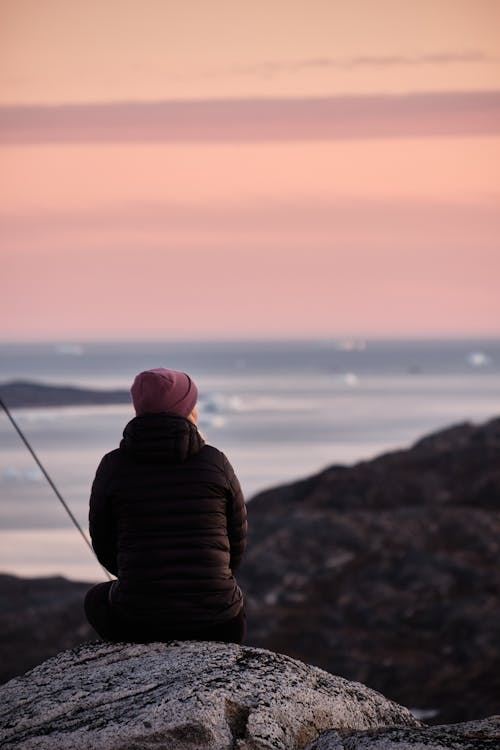 Anonymous traveler on stone contemplating sea at sunset