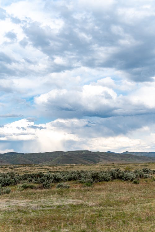 Scenery view of grass meadow behind ridge under sky with shining clouds in daytime