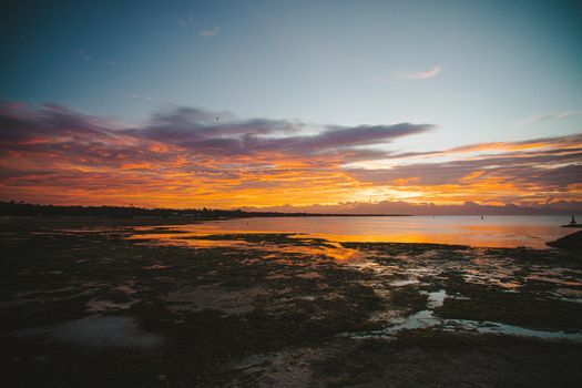 Spectacular view of colorful cloudy sky above sea and mounts near uneven terrain at sundown