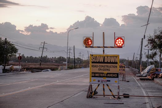 Twilight road construction with warning signs and lights cautioning drivers to slow down.