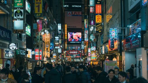 Free Many smiling ethnic people on city street between buildings with colorful signboards at night Stock Photo