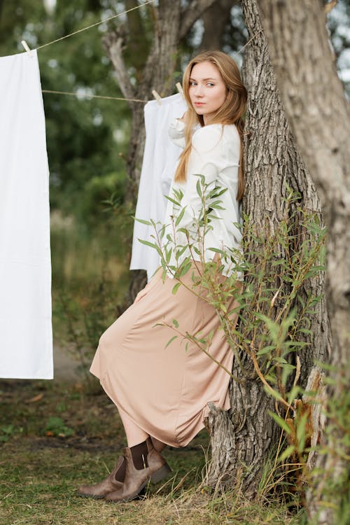 Woman in White Long Sleeve Shirt Leaning on Tree