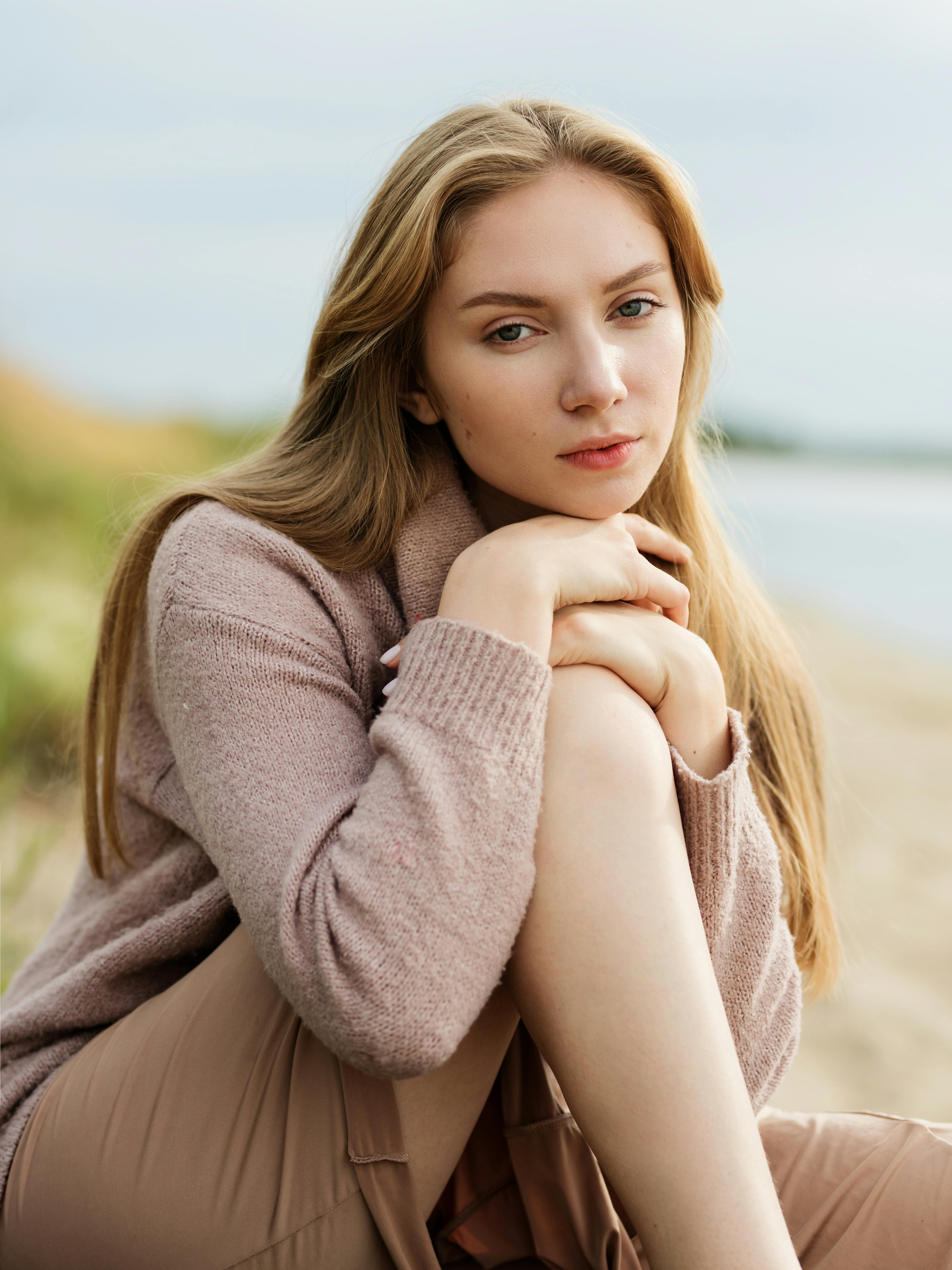 一个微风轻拂的日子里，一位穿着毛衣的白人妇女坐在海滩边，陷入了沉思