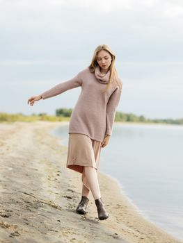 一位穿着毛衣和裙子的女人，优雅地沿着宁静的湖滨海滩行走