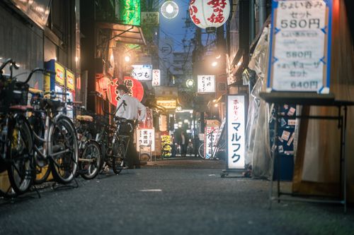 Free Lively night street scene in Osaka, Japan, featuring bicycles, lanterns, and illuminated storefronts. Stock Photo