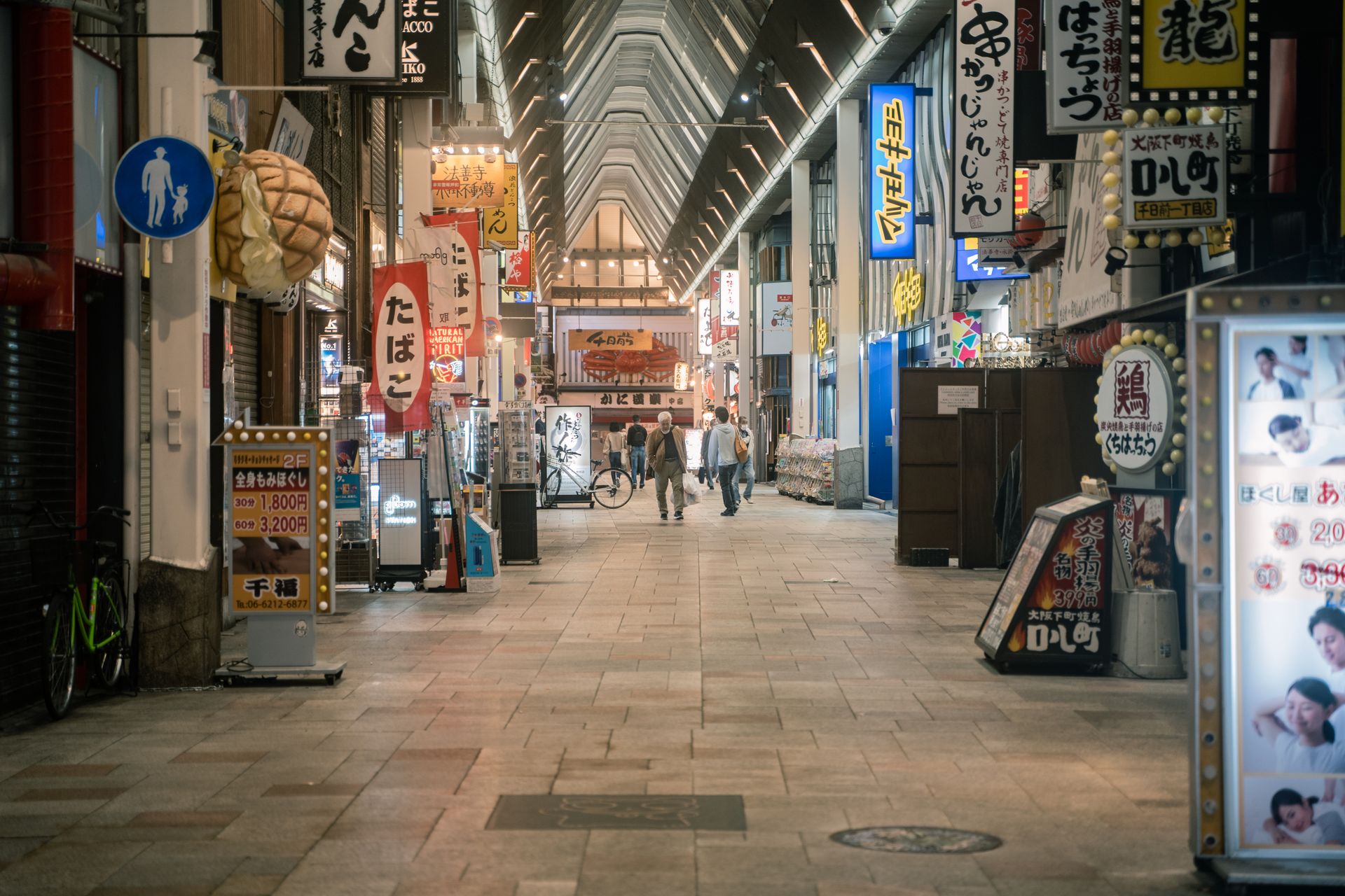 Bustling pedestrian street in Osaka lined with colorful shop signs and people walking at night.