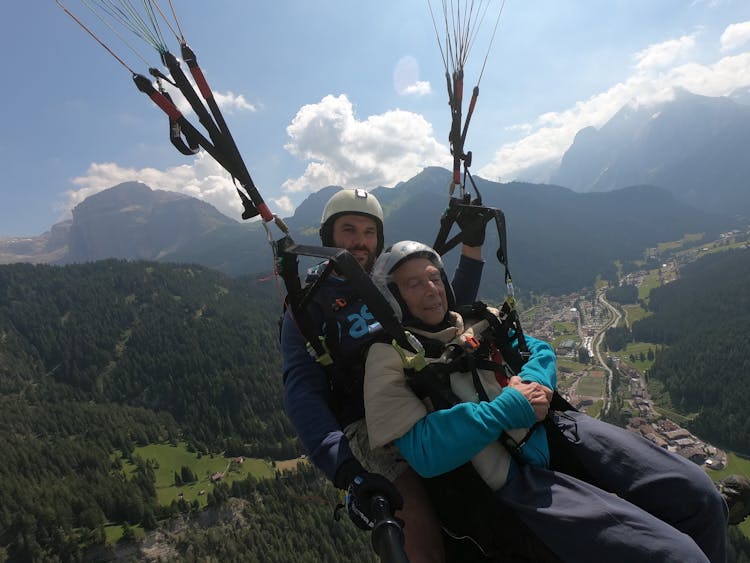 Senior Man With Instructor Parachuting Above Green Mountains